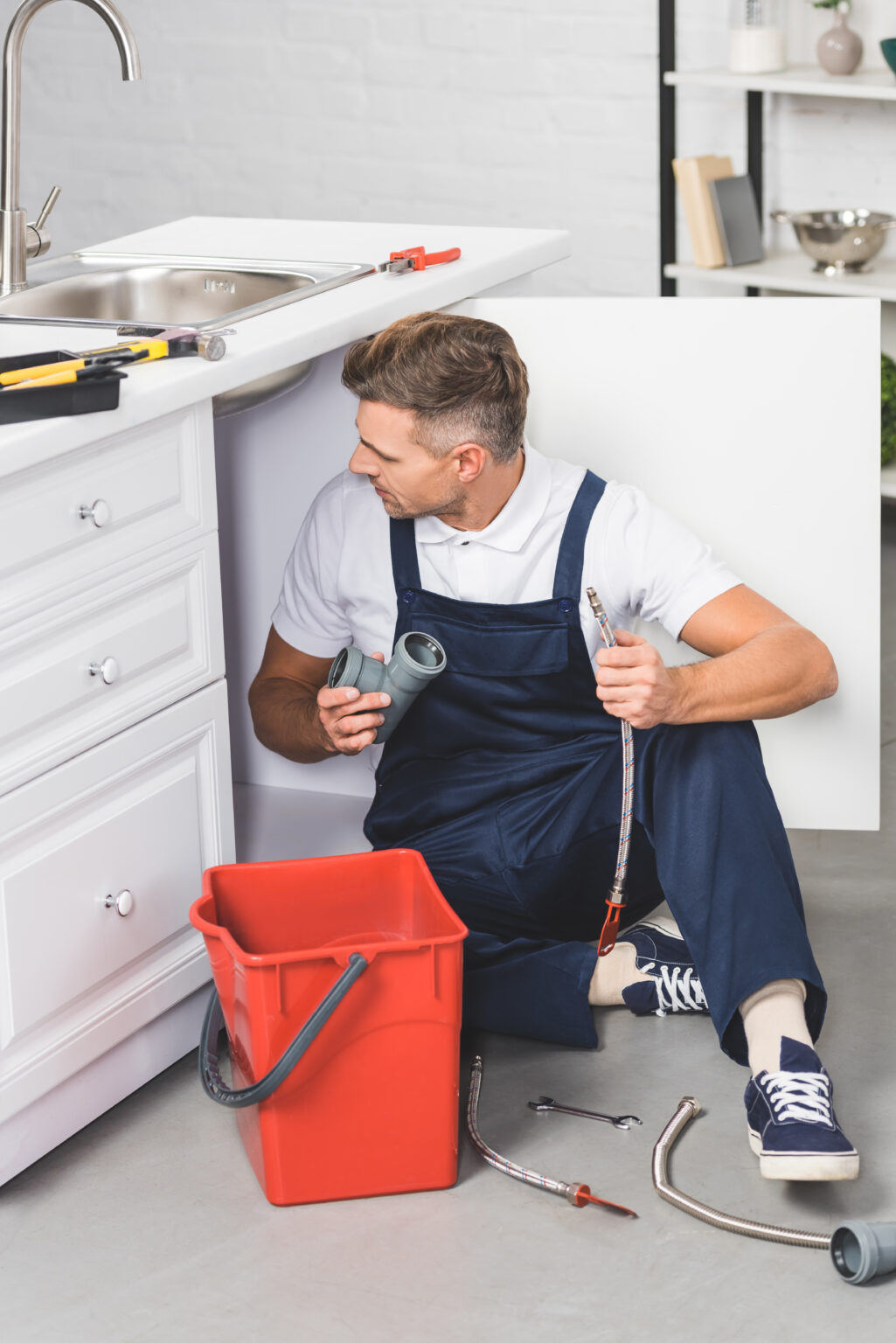 adult repairman with red plastic bucket holding pipes for repairing kitchen sink