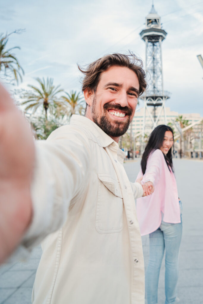 Vertical. Handsome young adult man walking and taking a selfie portrait holding his girlfriend's